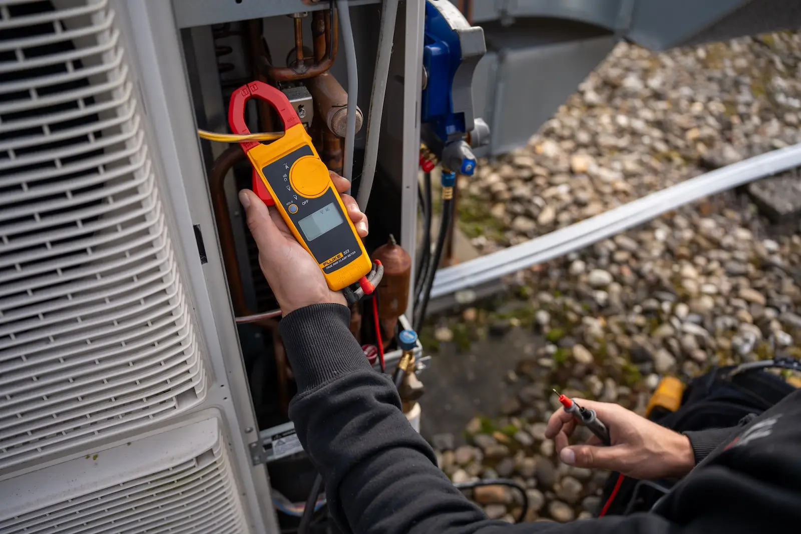 Monteur van Jadikoel meet met een stroomtang de elektrische aansluiting van een buitenunit