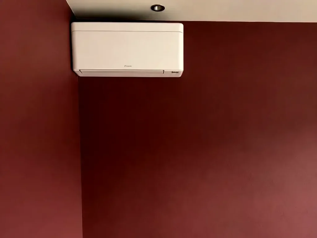 Daikin airco binnenunit hoog aan een donkerrode wand in een woning in Voorburg