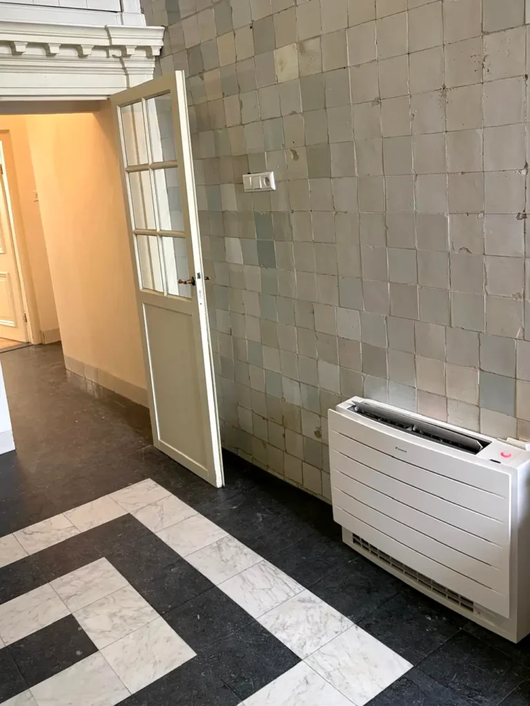 Daikin vloerunit tegen een historische tegelwand in de gang van een monumentaal pand in Den Haag